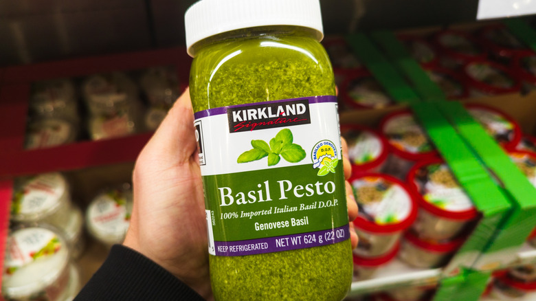 Hand holding jar of Kirkland Signature pesto in Costco refrigerated section