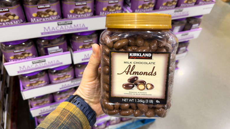 Hand holding container of Kirkland Signature chocolate covered almonds in Costco aisle