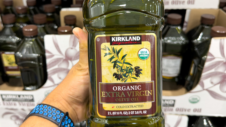 Person holding Kirkland Signature bottle of organic extra virgin olive oil