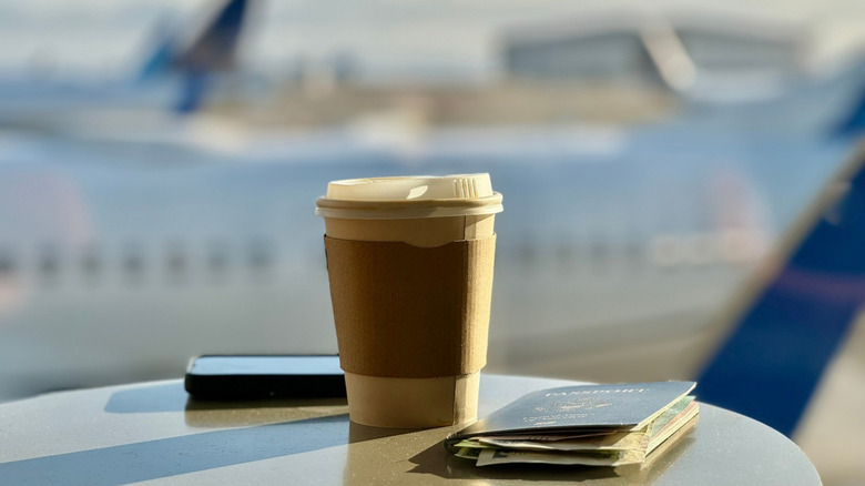 Coffee and passport on a table with airplanes in the back