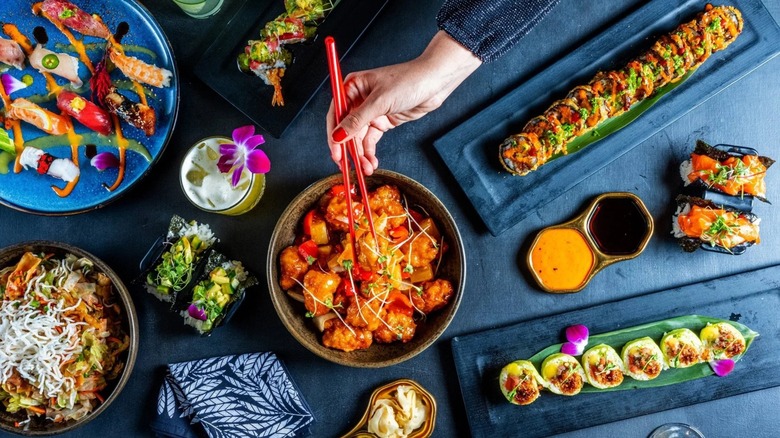 Table filled with assorted Asian dishes with a hand holding chopsticks