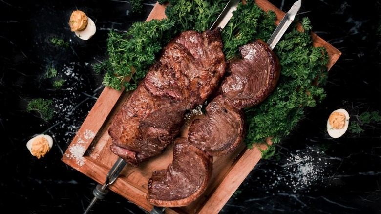Meat on skewers with parsley on wooden cutting board
