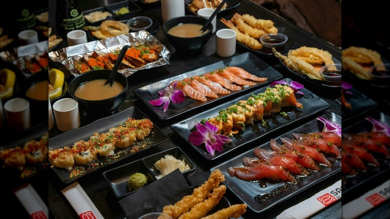 Assortment of suchi dishes on black plates with sauces