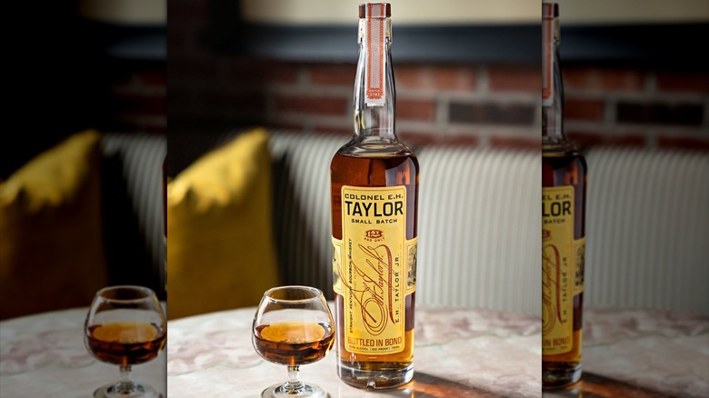A bottle of E. H. Taylor Small Batch on a table next to a filled glass