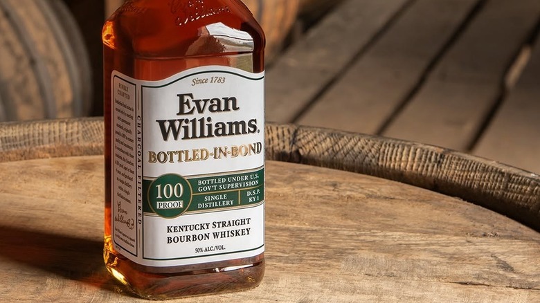 A bottle of Evan Williams Bottled-in-Bond posed on top of a wooden barrel