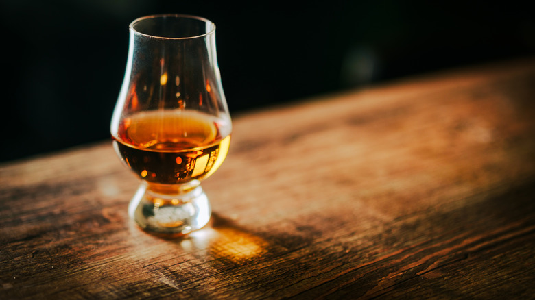 A filled Glencairn glass of whiskey shown on a wooden surface with light shining through