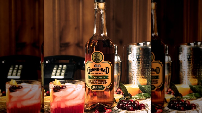 A bottle of Old Grand-Dad Bonded surrounded by fruits and a cocktail, with a wired telephone in the background