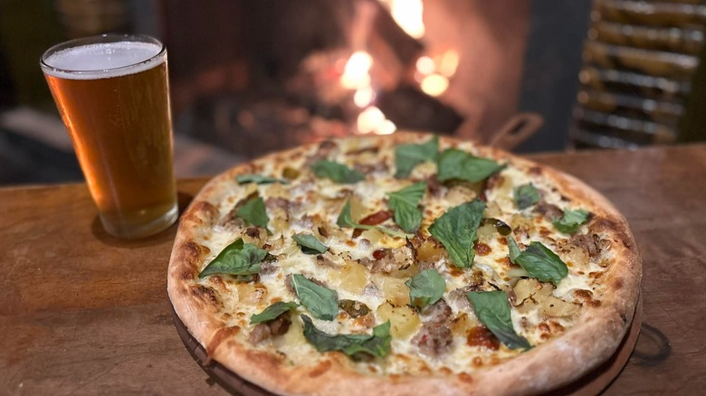 Pint of beer and wood-fired pizza in front of open fireplace