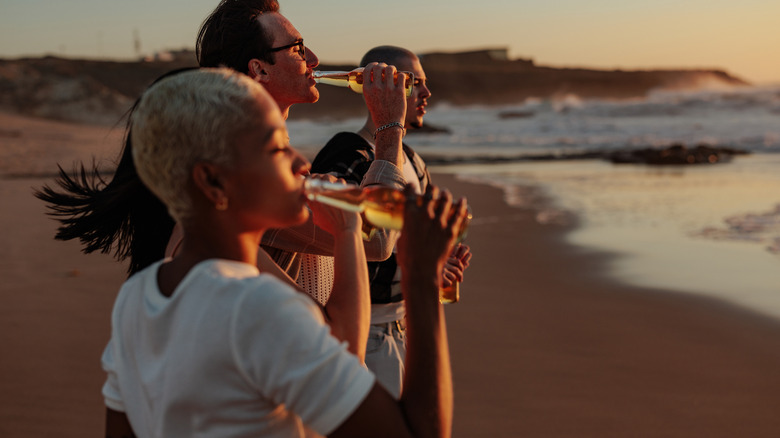 People standing on the beach drinking beers at sunset