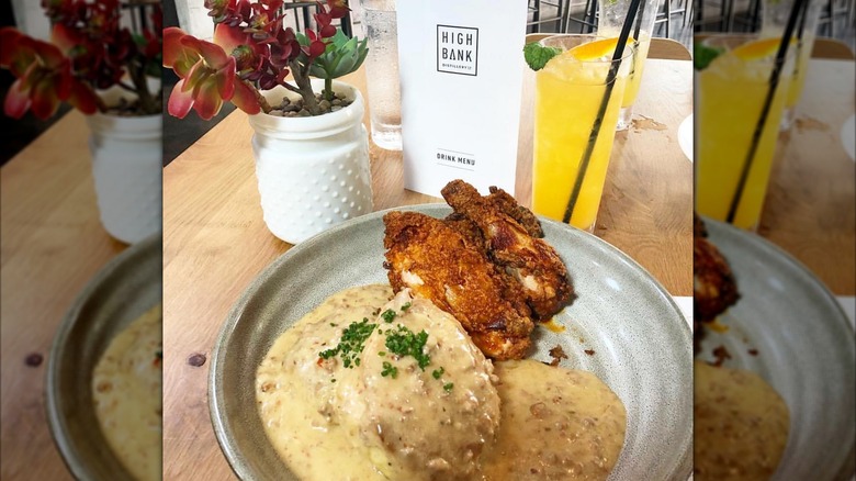 Plate of chicken, biscuits, and gravy on table with drink and menu