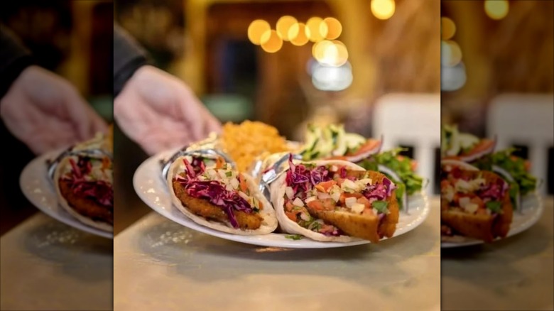 Fish tacos on a white plate being placed on a table