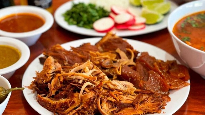 Carnitas on a white plate, surrounded by salsa bowls and other Mexican dishes
