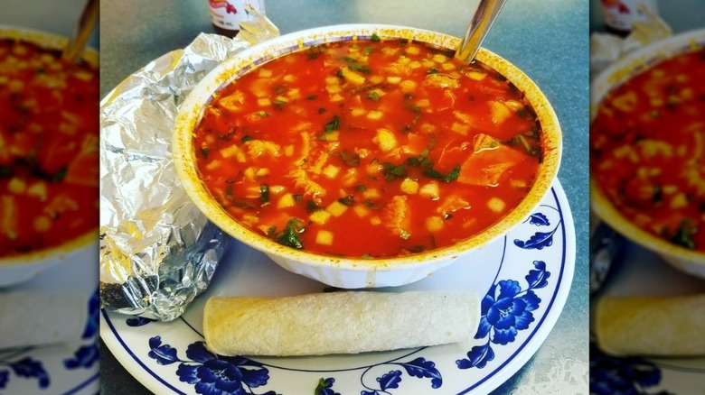 Large bowl of red pozole soup, served with fresh tortillas