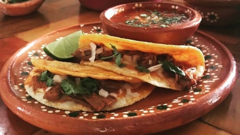 Two tacos filled with barbacoa, cilantro, and onions, served with a bowl of salsa