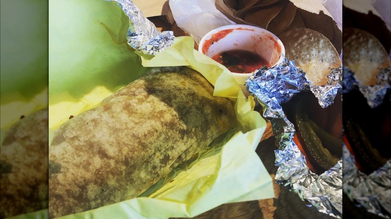 Close-up of a burrito and a side of salsa on paper and foil wrapping