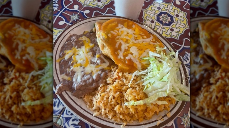 Refried beans topped with cheese, yellow Mexican rice, lettuce, and chile relleno with enchilada sauce