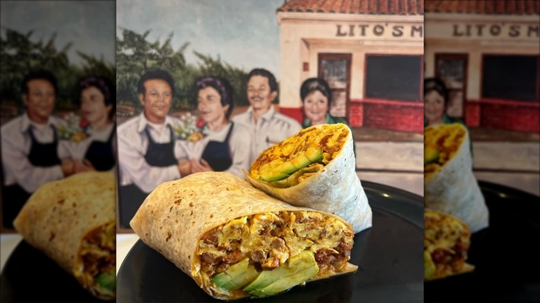 Burrito cut in half, filled with avocado, eggs, and chorizo, plated in front of a mural wall painting