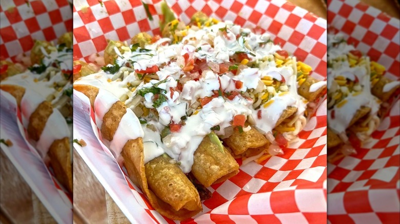Several rolled tacos topped with cilantro, tomato, and white sauce