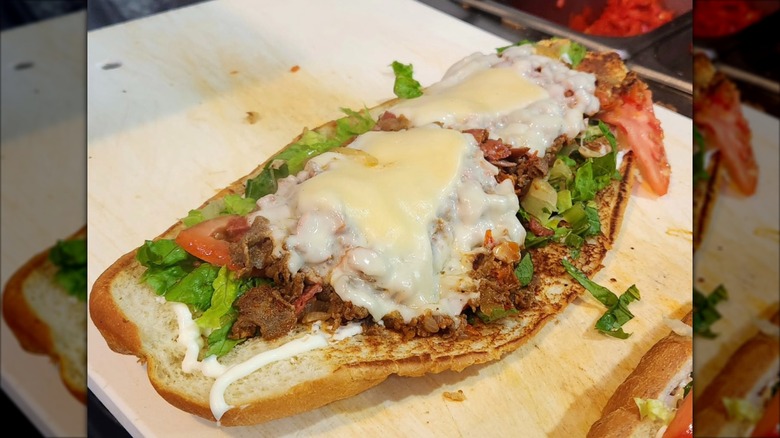 Italian steak sandwich covered in melted cheese on a wooden board from Gino's Deli Stop N Buy