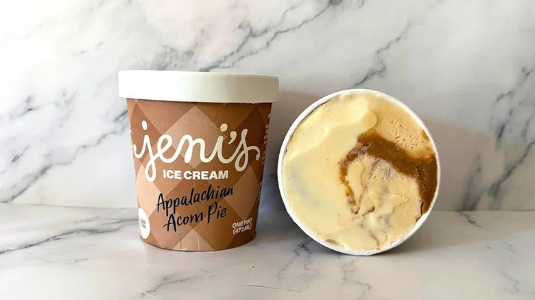 A sealed pint of Jeni's Appalachian Acorn Pie Ice Cream next to an upturned, open pint showing the cream and brown swirled ice cream inside