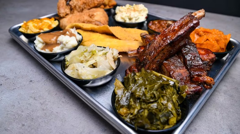 Tray with assorted food including ribs, collard greens, and mashed potatoes