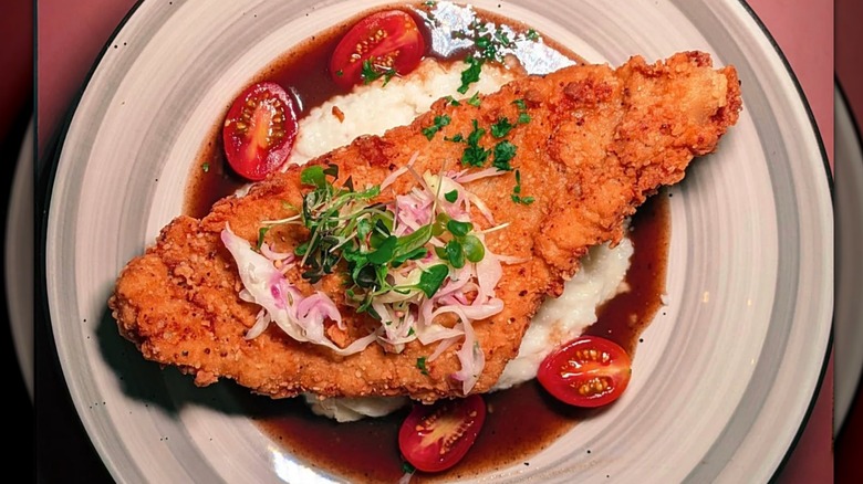 plate of shrimp and grits with piece of fried fish and sliced tomatoes