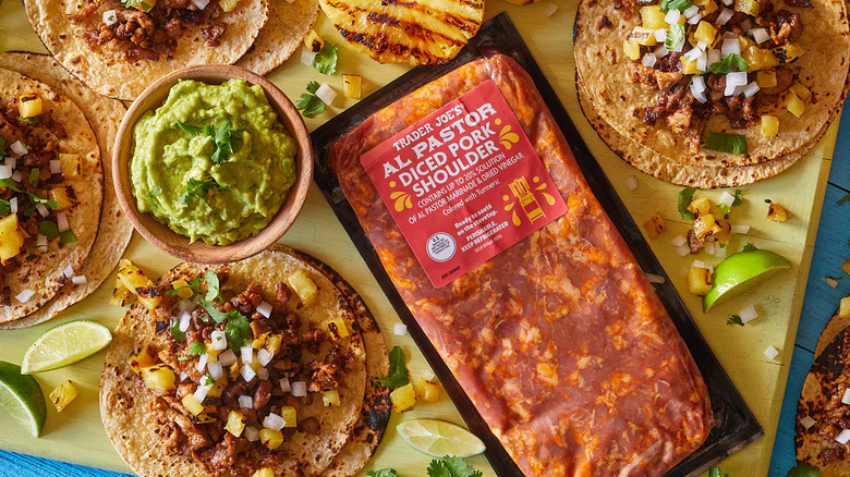 Package of Trader Joe's Al Pastor Diced Pork Shoulder next to bowl of guacamole and tacos with pork, onion, pineapple, and cilantro
