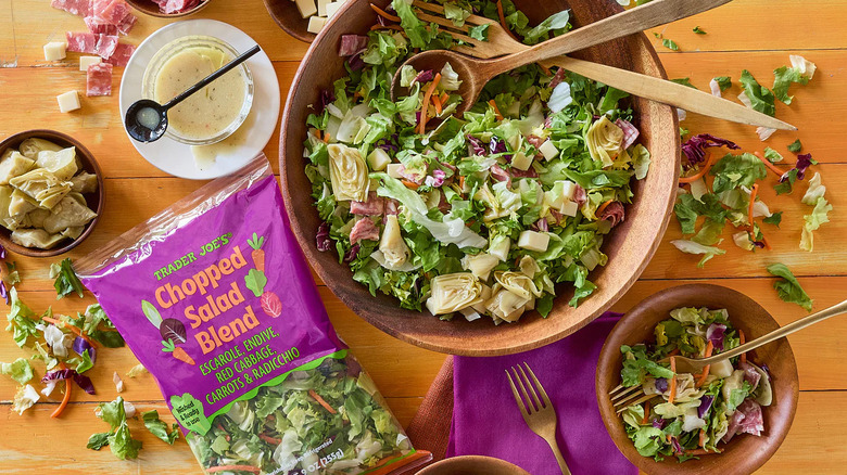 Bag of Trader Joe's Chopped Salad blend next to bowls of salad, dressing, and artichoke hearts
