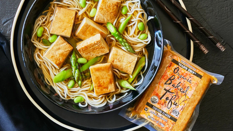 Package of Organic Baked Tofu Teriyaki Flavor next to black bowl of noodles, edamame, and tofu slices