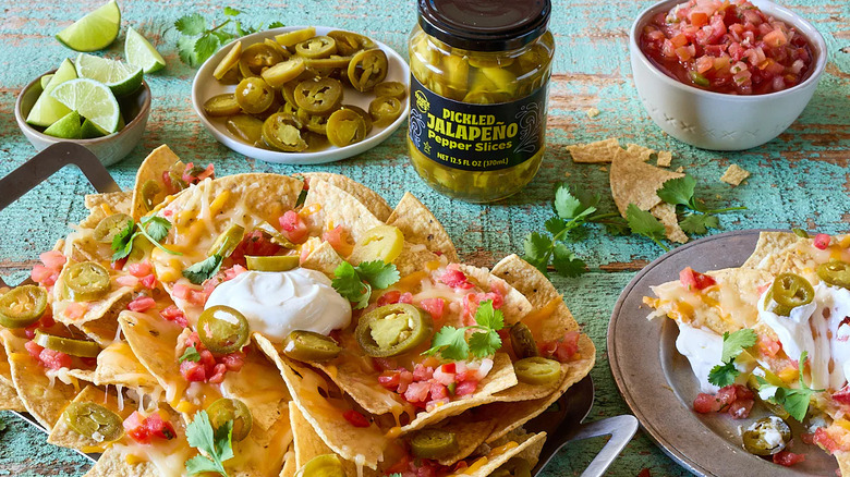 Trader Joe's Pickled Jalapeño Pepper Slices next to bowls and plates of nachos, salsa, and lime wedges