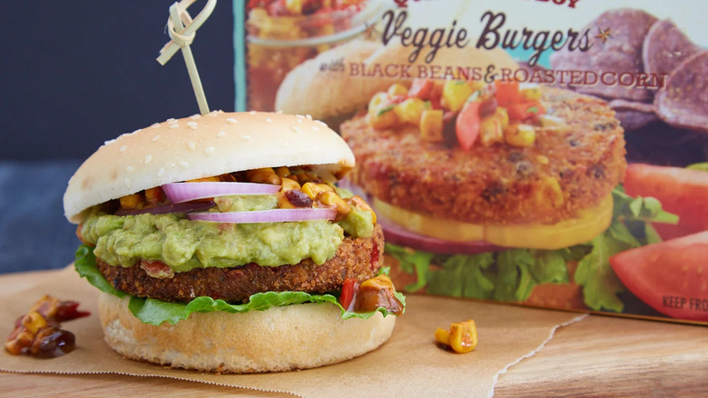 Box of Trader Joe's Quinoa Cowboy Veggie Burgers next to burger with lettuce, red onion, corn, and gucamole