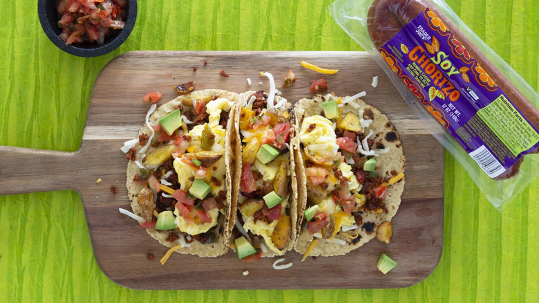 Package of Trader Joe's Soy Chorizo next to wooden board holding three chorizo tacos with avocado