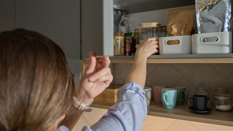 erson takes jar from kitchen shelf filled with food containers and glassware