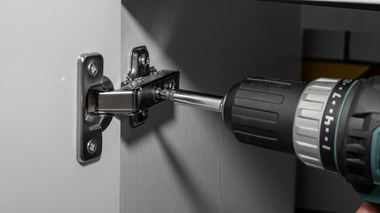 Kitchen hinge being screwed to the cabinet with a drill