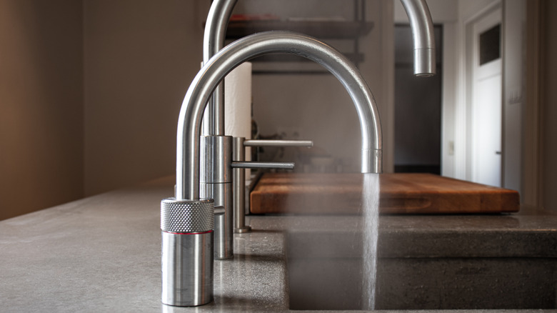 two silver metal arched taps over kitchen sink, closest is pouring out steaming water