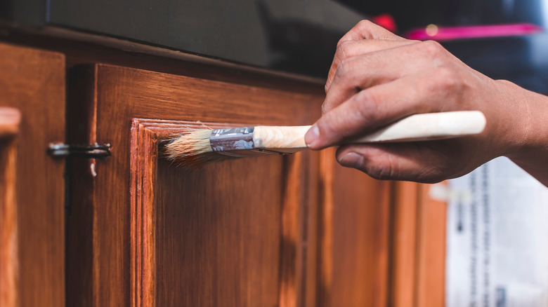 hand paints a fresh coat of varnish on the surface of a base kitchen cabinet