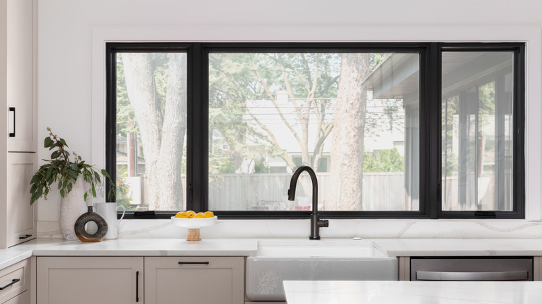 large black window behind white farmhouse sink with black tap and marbled countertop