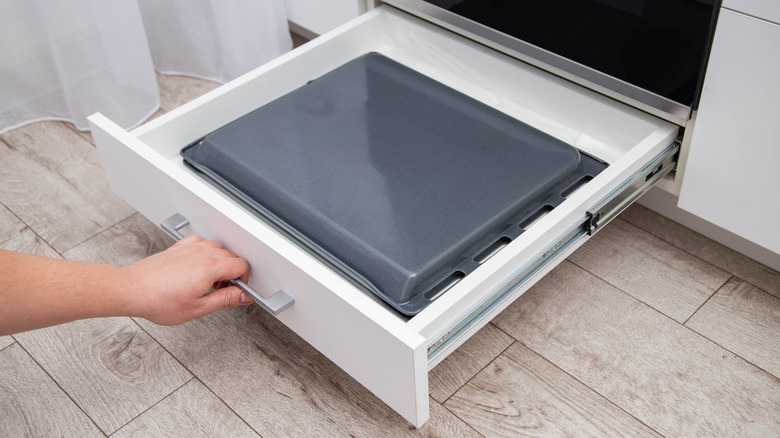 hand pulls out a drawer with baking sheets in the kitchen