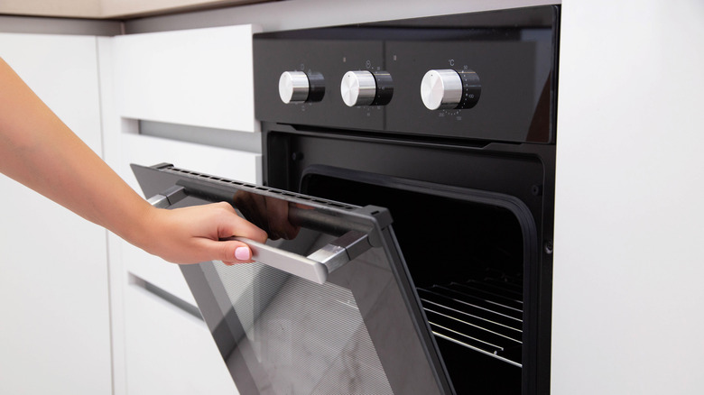 A woman's hand opens the door of a black electric convection oven