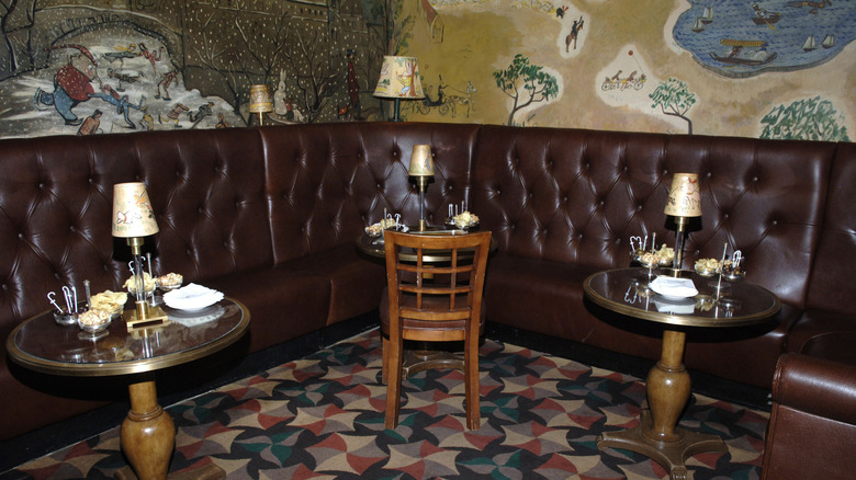 Tables and chairs against a leather booth and illustrated wallpaper.
