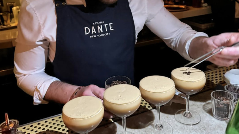 a man in a Dante apron placing espresso beans on a row of martinis.