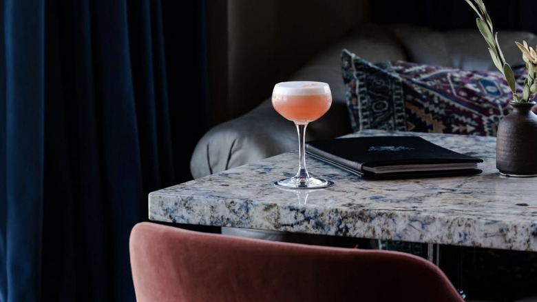a lone martini on a marble bar with a plant in the background.