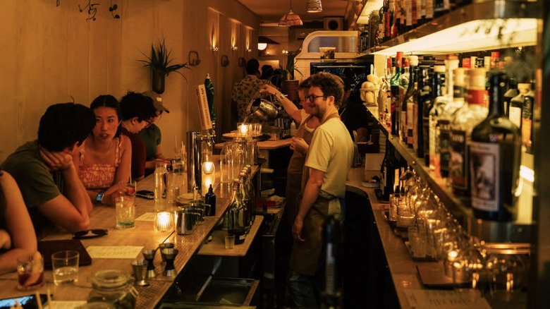 candelit bar with people at the bar and bartenders behind the counter.