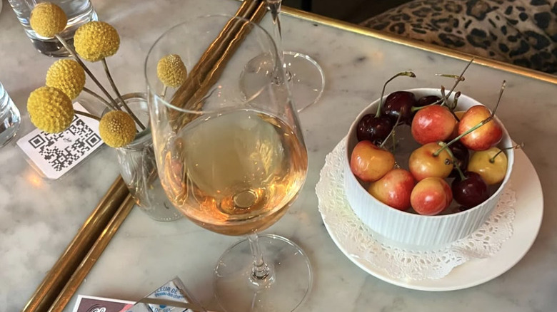 a glass of white wine next to a bowl of white cherries.