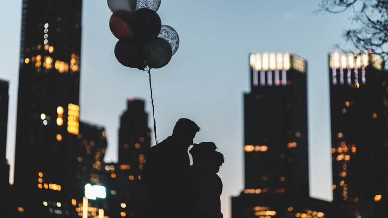 a silhouette of a couple holding balloons against a NYC skyline at night.