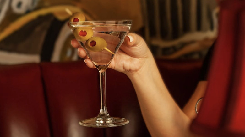 a woman's hand holding up a martini glass with three olives.