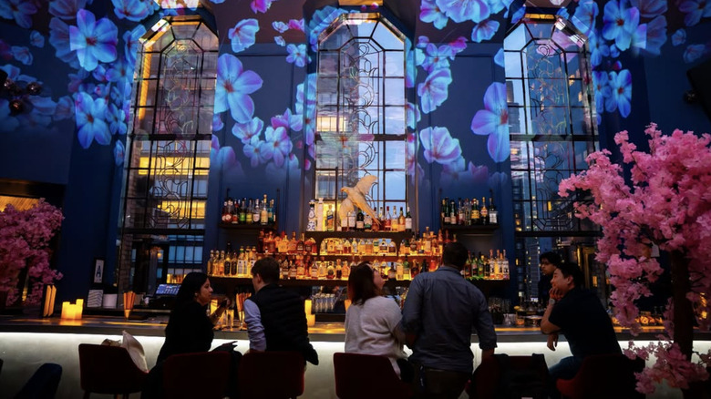 People sitting at a lit up bar with flora projections on the wall.