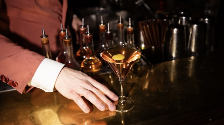 a hand pushing a martini cocktail across a bar.