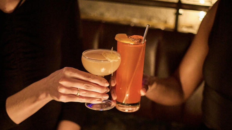 Two hands holding a cocktail and toasting.