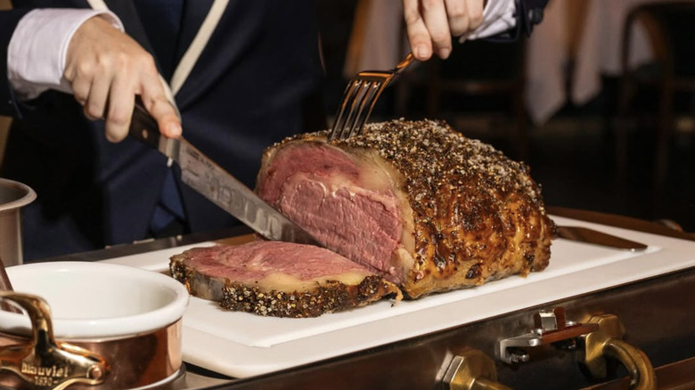 A man cutting off a large slab of beef on a white platter